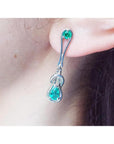 Love knot emerald earrings with pear-shaped Colombian emeralds in 14K white gold on an ear.