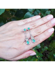 14K white gold love knot earrings with pear-shaped Colombian emeralds, held in a hand.