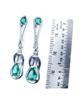 14K white gold love knot emerald earrings with pear-shaped Colombian emeralds, shown next to a ruler.