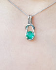 A white gold pendant with a round cut natural emerald on a chain, worn around the neck.