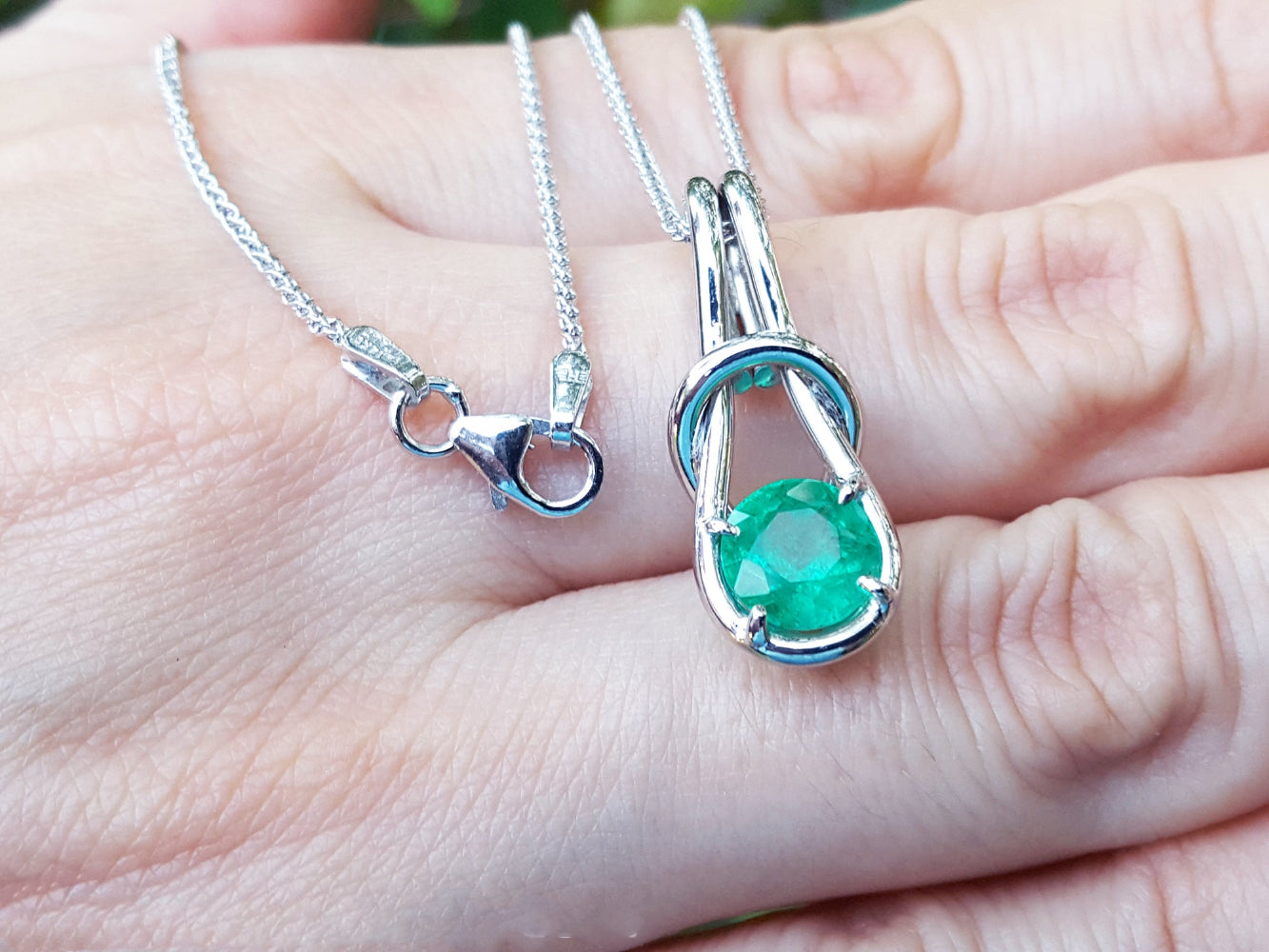 White gold pendant with a round cut emerald held on a hand.