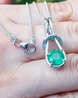 White gold pendant with a round cut emerald held on a hand.