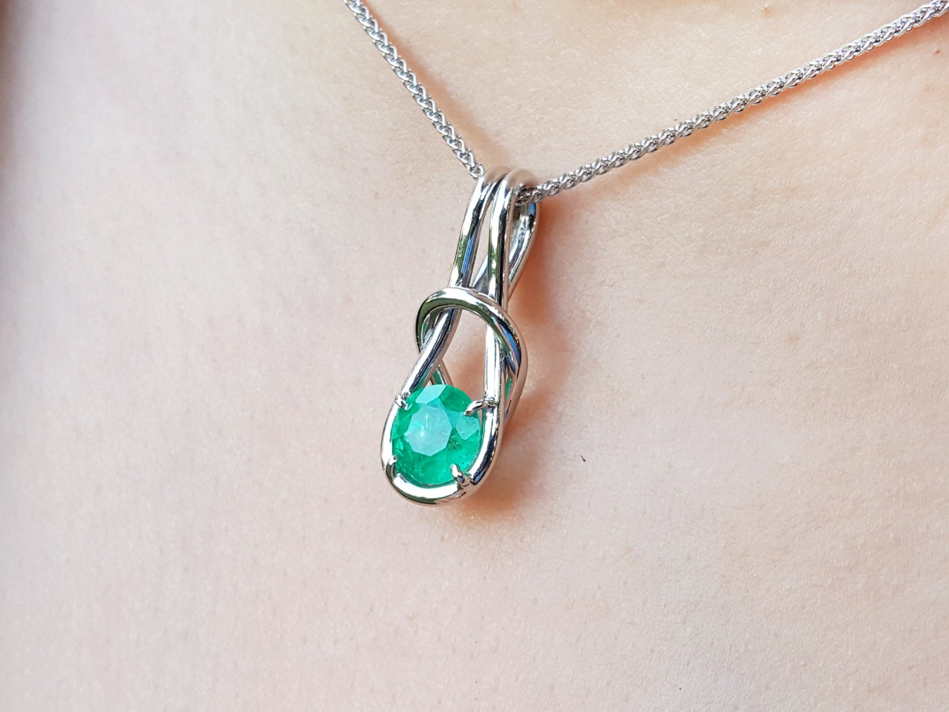 White gold emerald love knot pendant necklace on light skin background.