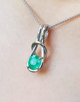 White gold emerald love knot pendant necklace on light skin background.