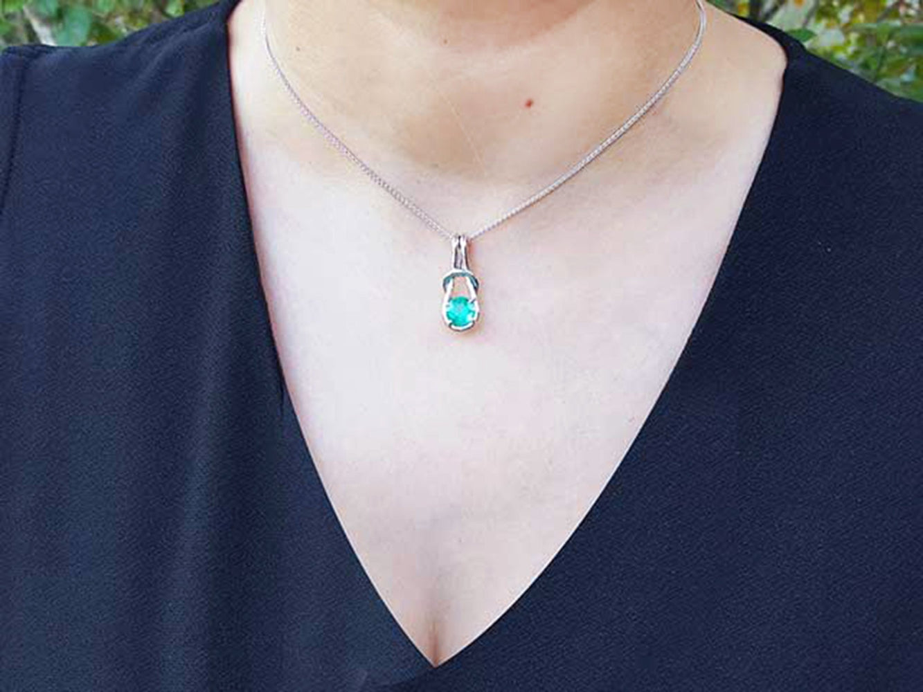 White gold necklace with a round cut emerald pendant on a person wearing a black top.