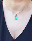 White gold necklace with a round cut emerald pendant on a person wearing a black top.