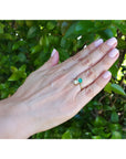 Hand wearing a two stone emerald and diamond ring in yellow gold.