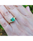 18K yellow gold three-stone ring with a vibrant Colombian emerald and two trillion-cut diamonds on a hand.