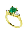 18K yellow gold three-stone ring with a vibrant emerald and two trillion-cut diamonds.