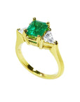 18K yellow gold three-stone ring with a vibrant emerald and two trillion-cut diamonds.