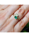 A close-up of a hand wearing two gold rings, one with a rectangular green emerald-cut gemstone and the other with a smaller round green stone.