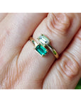 A close-up of a hand wearing a gold ring with two rectangular emerald-cut green gemstones.