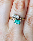 A close-up of a hand wearing a you and me 18k gold ring with a natural emerald rectangular emerald-cut and diamonds.