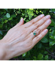 A you and me 18k yellow gold you and me ring worn on a person's ring finger against a background of green foliage.