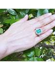 Anillo de oro blanco 18K con esmeralda colombiana rectangular de 3.98 ct. rodeada de diamantes en mano.