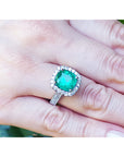 Una mano vistiendo un anillo con esmeralda corte cojín rodeada de diamantes en oro blanco.