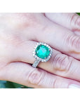 Una mano vistiendo un anillo con esmeralda corte cojín rodeada de diamantes en oro blanco.
