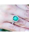 Anillo de oro blanco 14k con esmeralda colombiana corte cojín de 3.92 ct y halo de diamantes en mano.