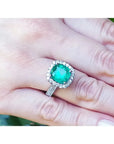 Anillo de oro blanco 14k con esmeralda colombiana corte cojín de 3.92 ct y halo de diamantes en mano.