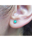 An earlobe wearing a martini emerald stud earring in white gold.