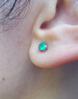 A woman's ear wearing a three pong set martini emerald stud earrings.