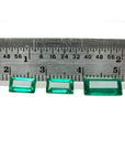 Three baguette-cut natural loose Colombian emeralds, deep bluish-green, displayed with a ruler for scale.