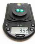 Matched pair of 3.62 carat pear-cut bluish-green Colombian emeralds on a black digital scale.