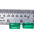Matched pair of natural emerald-cut green emeralds next to a ruler for scale.