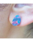Close-up of a colorful teardrop-shaped Australian opal earring worn on an ear.