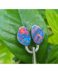 Matching pair of 4.72 ct Australian doublet opals with red, blue, and green flashes on a green leaf.