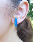 Close-up of an ear wearing a blue opal earring with a blurred green background.