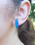 Deep blue doublet opal earring with green flashes, worn on an ear.