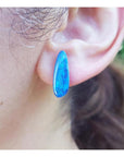 Deep blue Australian doublet opal earring with green flashes, worn on an ear.
