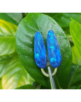 Blue opal earrings on a green leaf with a blurred green background.