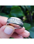 Natural diamond band ring for men in 14K white gold, held by fingers against a blurred green leafy background