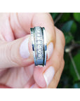 Natural diamond band ring for men in 14K white gold, held between fingers against a blurred green background.