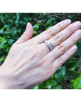 Hand wearing a diamond band ring for men with a green leafy background