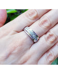Natural diamond band ring for men in 14K white gold, on a person's finger against a blurred green background