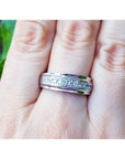 Natural diamond band ring for men in 14K white gold, on a finger against a blurred green background