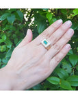 Men's 14K yellow gold ring with a bezel-set emerald gemstone framed by diamonds, worn on a hand.