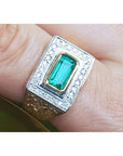 Men's gold ring with emerald and diamond accents on a finger.
