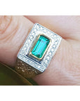 Men's gold ring with emerald and diamond accents on a finger.