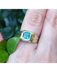 Gold pinky ring for men with a natural colombian emerald on a finger against a natural background.