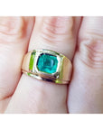 A men’s solitaire ring featuring a square natural Colombian emerald, bezel-set in 14k gold, worn on the hand.