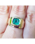 A men’s solitaire ring featuring a square natural Colombian emerald, bezel-set in 14k gold, worn on the hand.