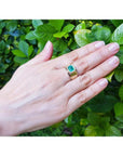 Men's 14K yellow gold solitaire ring with a bezel-set, medium green emerald on a hand.