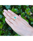 Hand wearing a mens horseshoe ring with a natural colombian emerald against a green leafy background.