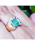 A men's emerald horseshoe ring with accent diamonds in yellow gold on a hand between fingers.
