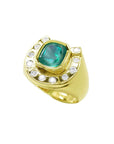 Gold horseshoe ring with a natural colombian emerald and diamond accents on a tilted position topside view.