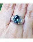 White ring with a blue natural sapphire oval cut on a finger against a natural background